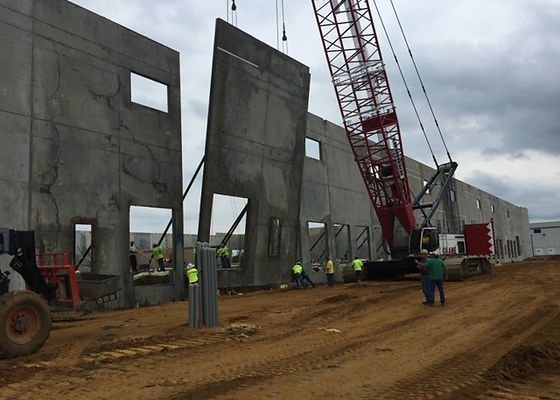 Tall concrete wall panels being raised by crane on a large commercial site
